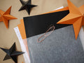 A styled flat-lay of craft materials featuring orange and black star-shaped paper cutouts, sheets of black and orange paper. Whimsigoth fun easy halloween crafts.with this DIY paper star garland kit.