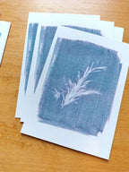 A stack of small bluish art riso prints featuring a unique cyanotype of rosemary.