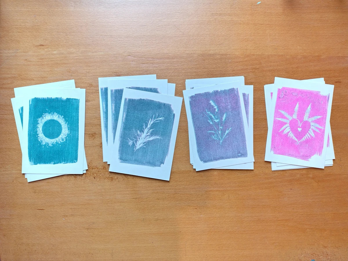 Four small art riso prints laid out on a wooden table. Each showing a unique cyanotype printed in blue, purple and pink tones.