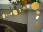 Gold circular sewn paper garland hanging on a fireplace mantel with greenery.