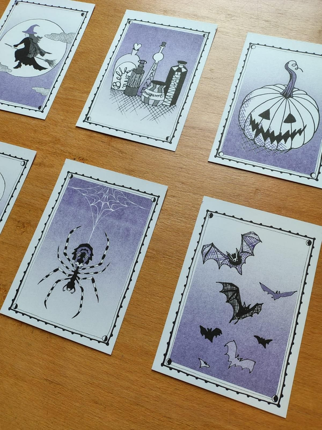Set of tarot style riso prints with Halloween-themed illustrations on a wooden surface with candles and a framed picture.