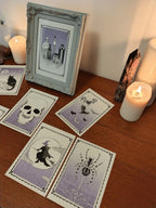 Halloween riso prints on a wooden surface with candles and a framed picture - witches, spiders, skulls, bats and potions