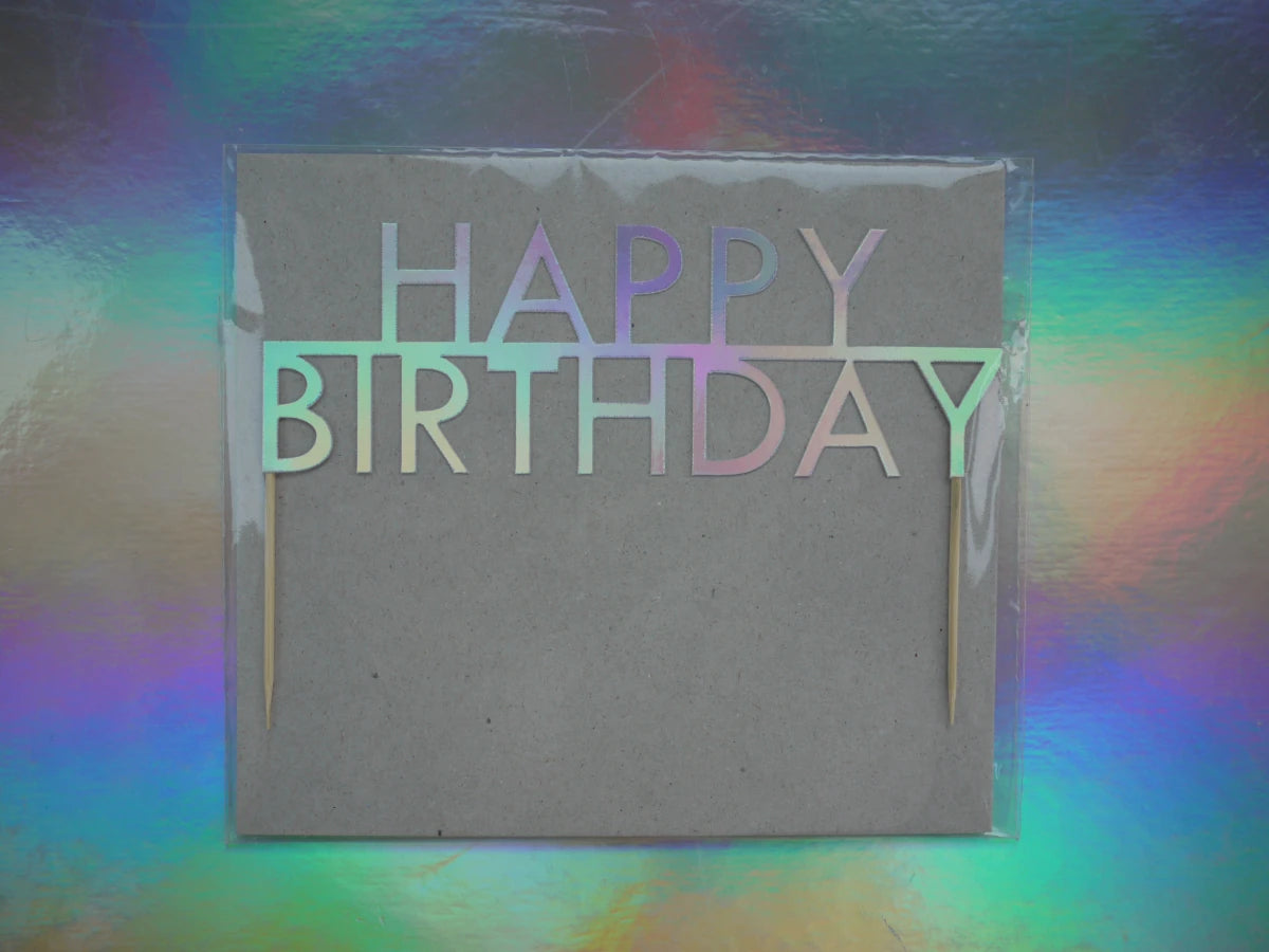 Holographic birthday cake topper that reads 'HAPPY BIRTHDAY,' photographed against a holographic rainbow background.