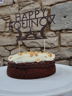 Cake with white frosting and a 'Happy Equinox' decoration on a stone background