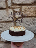 Happy equinox cake topper in a cake topper held against a stone wall