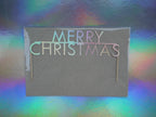 A 'Merry Christmas' cake topper with holographic card, set against a colourful holographic background.