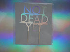 Birthday cake topper that says 'NOT DEAD YET' in holographic card. 