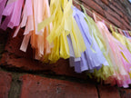 Close up pastel colourful tassel garland on a brick wall