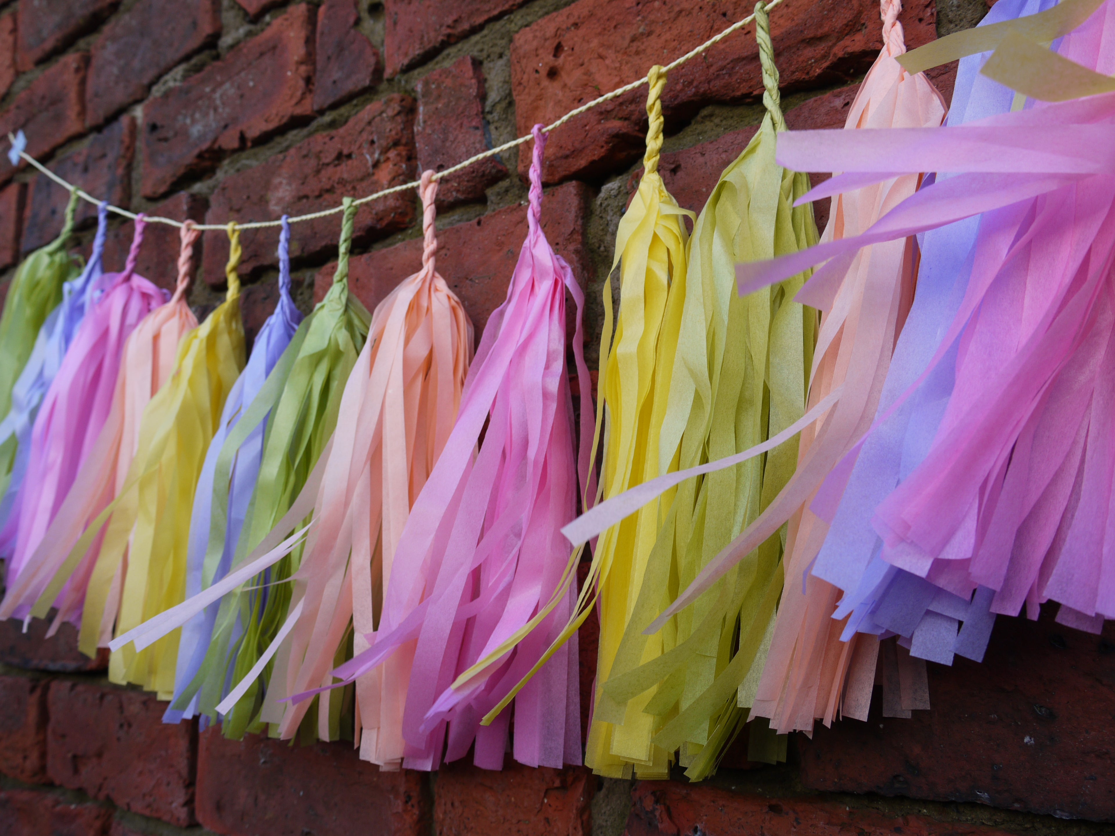 Pastel colourful tassel garland caught in the wind, on a brick wall