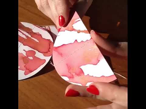 Process video of abstract ink painting, cut moon phases shapes, stitching the garland, end pieces glued on to garland. Finished garland moved to catch the light then rapped round greyboard for packaging