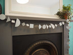 A silver geometric multi shape garland made of paper hanging across a dark fireplace mantel below a mirror. Fun easy party themes to take away the stress of decorating