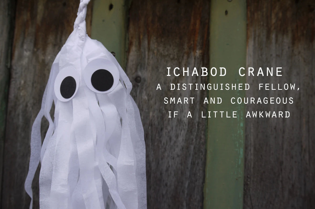 A spooky but cute white ghost Halloween decoration with large black eyes on a white tassel, photographed against a weathered wooden wall with white text on the right reading 'ICHBOD CRANE A DISTINGUISHED FELLOW, SMART AND COURAGEOUS IF A LITTLE AWKWARD'.